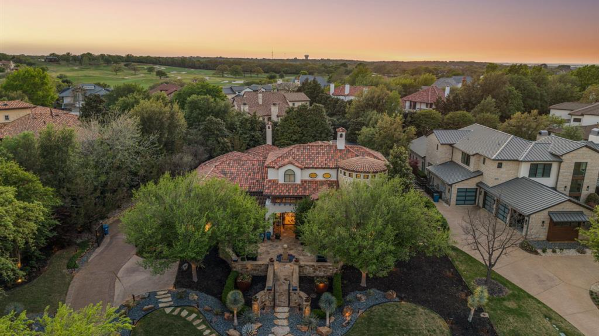 A private courtyard estate inside the guard gates of Vaquero at dusk, fire features glowing beside a reflecting pool.