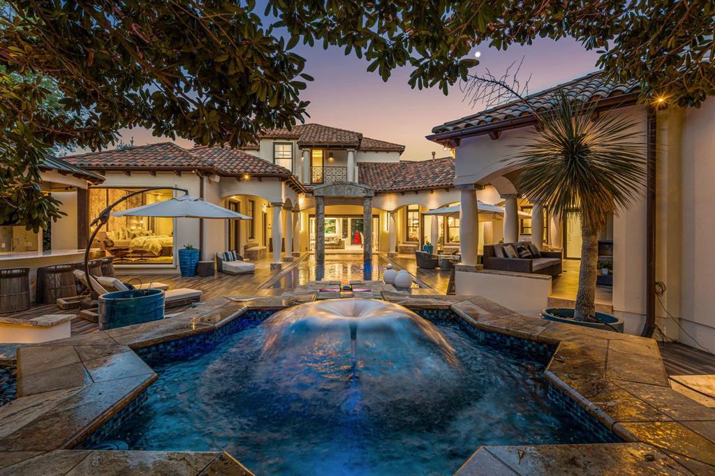 The backyard resort at dusk: a chilled courtyard pool with a bubbler fountain glowing blue, the U-shaped house wrapping around it, loungers and umbrellas, a moon in a lavender sky.