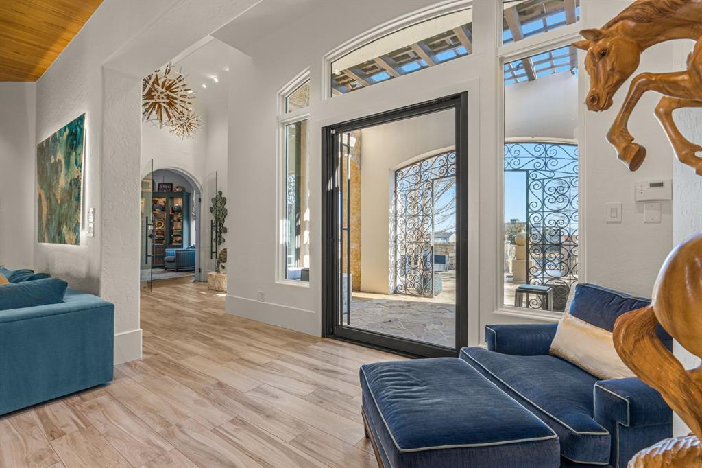 The entry hall and sitting area: white plaster walls, light wood floor, a carved wood leaping-horse sculpture, a sunburst chandelier, and sliding glass to the courtyard.