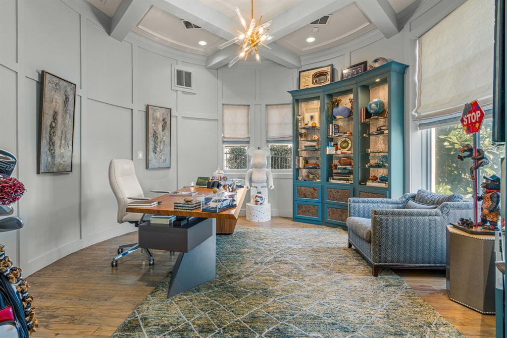 The office: a circular paneled turret room with a coffered ceiling, a sputnik chandelier, a walnut desk, teal glass display cabinetry, and curved windows to greenery.
