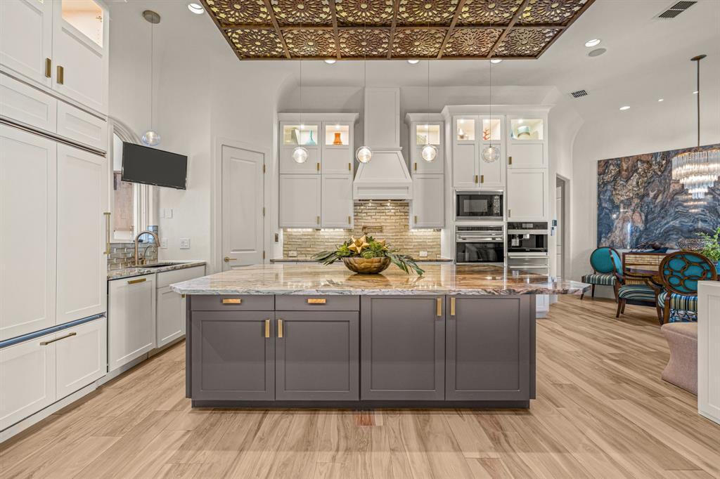 The chef's kitchen: a gray island with a book-matched stone waterfall counter, white perimeter cabinetry, a pierced gold ceiling panel, and glass-front upper cabinets.
