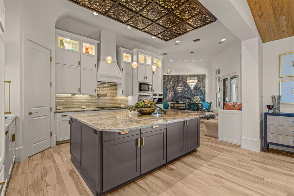 The kitchen looking toward the breakfast nook: the gray island and gold ceiling, with a sightline to the stone-slab-wall dining and its chandelier.
