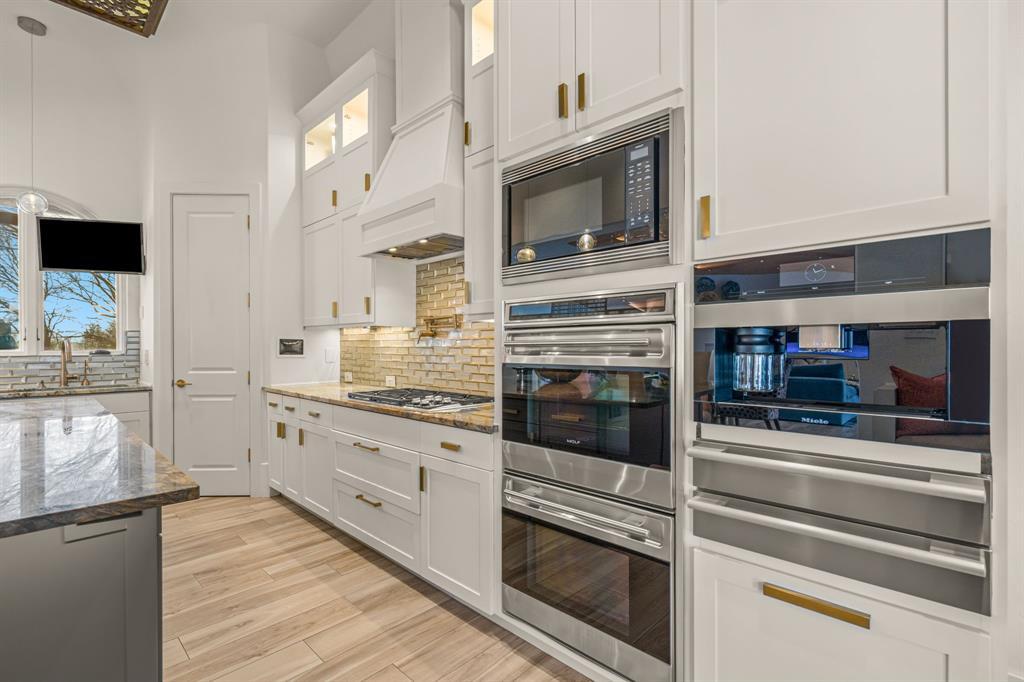 Appliance detail: stacked Wolf double ovens, a microwave, a Miele built-in coffee system, and a warming drawer set into white cabinetry with a stone backsplash.