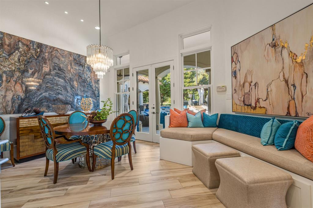 The breakfast and dining area: a crystal drum chandelier over a round table, a dramatic blue-and-copper stone slab feature wall, a built-in banquette, and French doors to the courtyard.