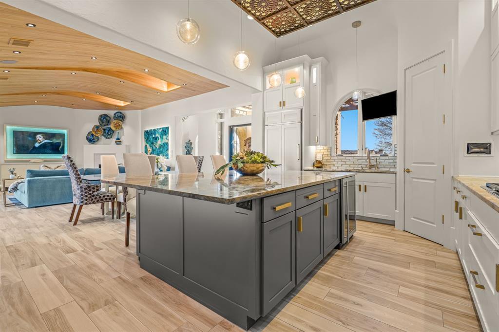An open-plan view: the kitchen island in the foreground opening to the wave-ceiling family and dining rooms beyond — the whole living core in one shot.