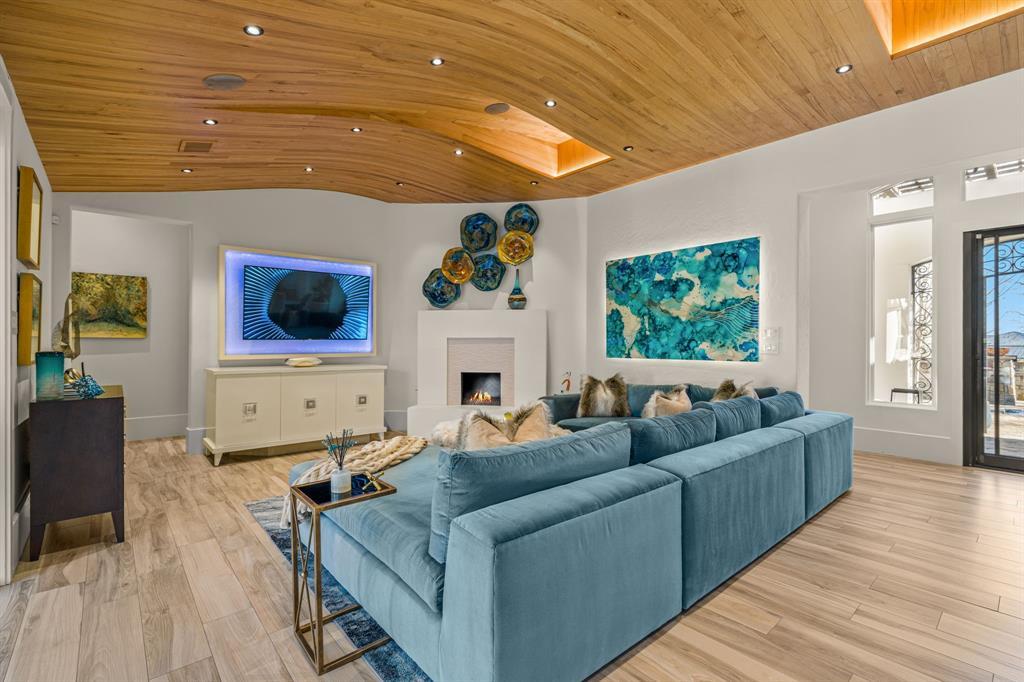 The family room from another angle: the backlit television wall, white fireplace, teal sectional, abstract art, and glass to the courtyard at right.