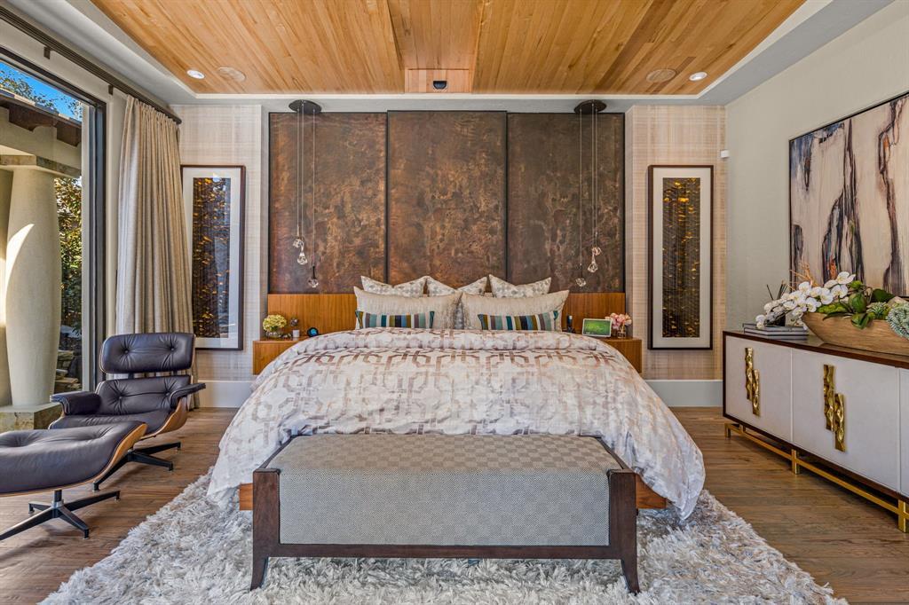 The primary bedroom head-on: the copper headboard wall centered, twin suspended pendants, framed art, a gold-accent credenza, and a wood-plank ceiling.