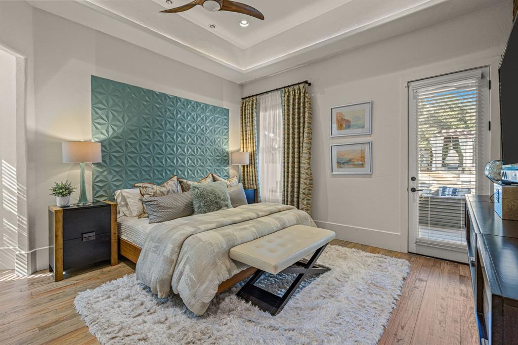 A secondary bedroom: a teal three-dimensional geometric accent wall, a tray ceiling, an upholstered bench, a French door to a balcony, and a hardwood floor.