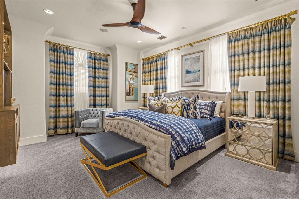 A secondary bedroom: a tufted linen sleigh-style bed, blue and green striped drapery on two window walls, and a mirrored nightstand.