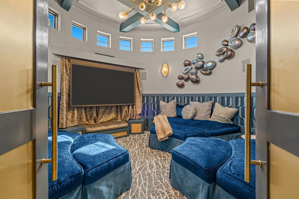 The circular media room: custom curved blue velvet seating following the round wall, a concealed motorized screen framed in drapery, a ring of clerestory windows, and a sputnik chandelier.